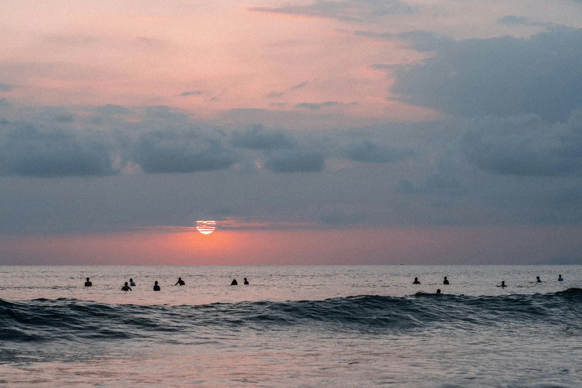 Surfers wait beyond a breaking wave as the sun sets over the ocean at Jacó.