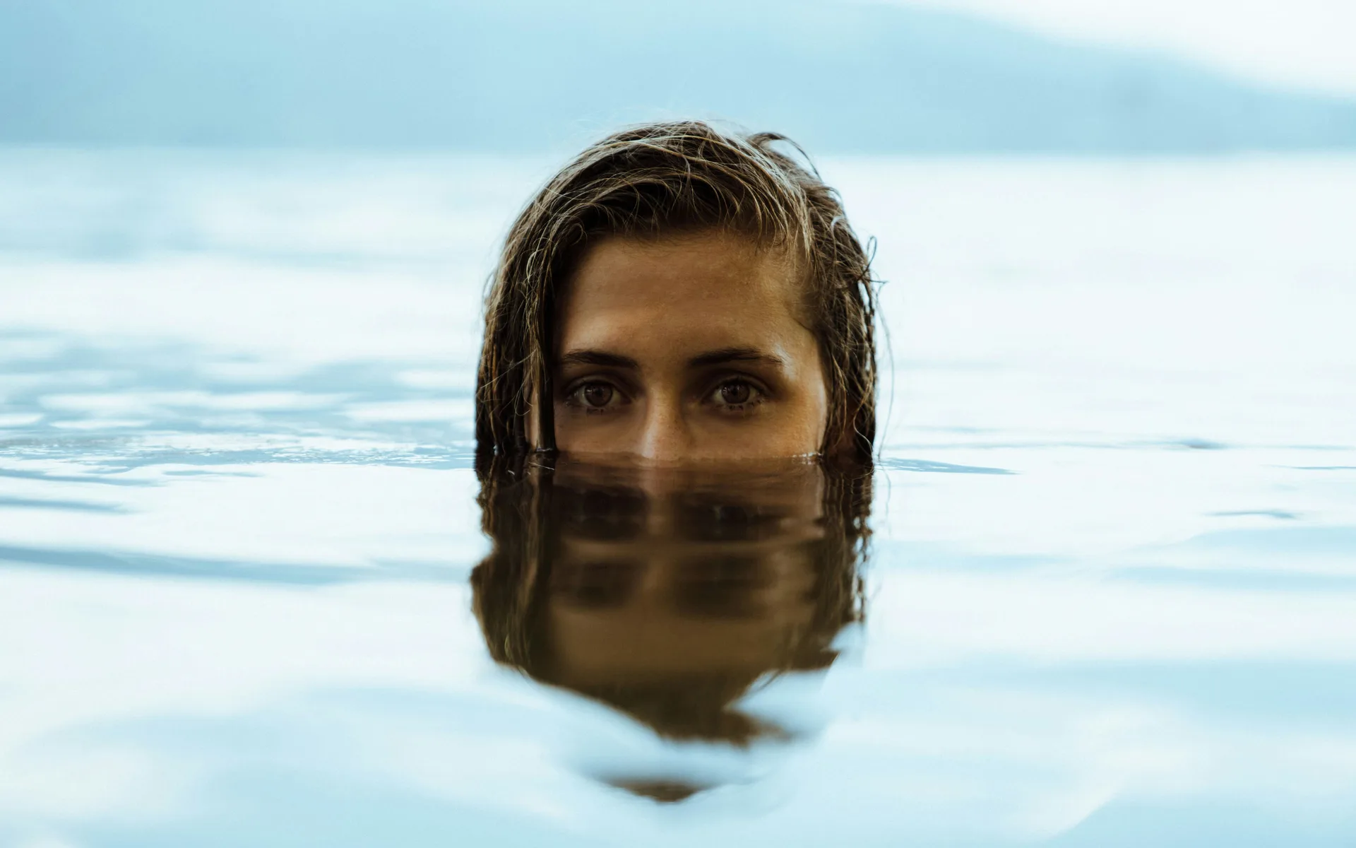 A woman resting in still water, only her eyes above the surface