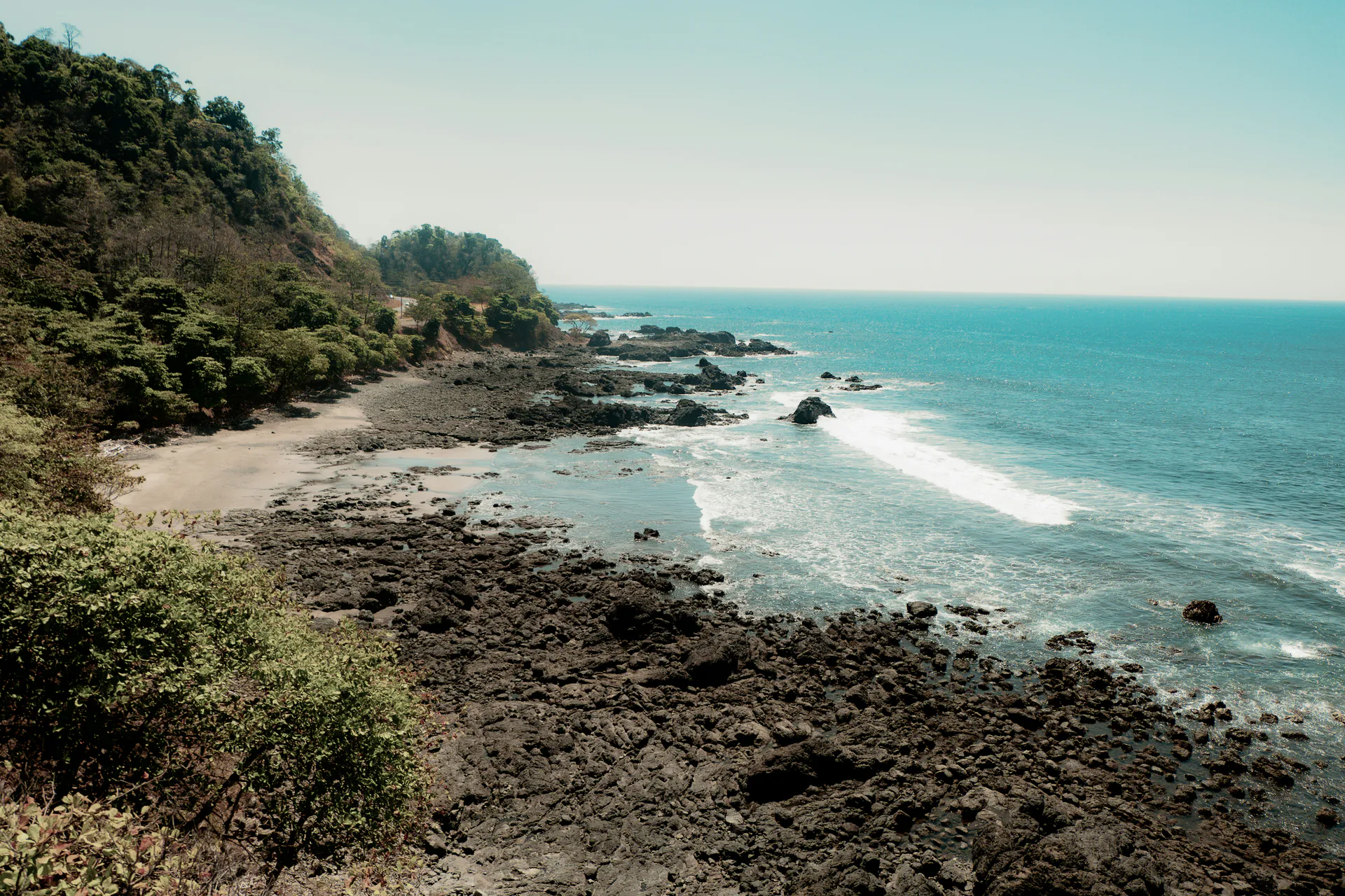 Wooded hills meet a rocky shoreline and Pacific surf near Jacó, Costa Rica.
